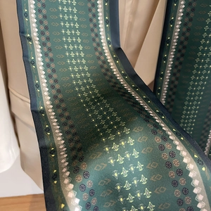 Gros plan sur un foulard étroit vert foncé avec motifs floraux et géométriques dorés