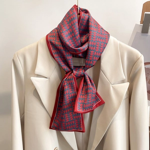 Détail d'un foulard en soie rouge et bleu-gris noué sur le revers d'un blazer écru