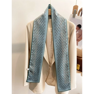 Détail d'un long foulard en soie bleu à motifs géométriques sur un blazer beige