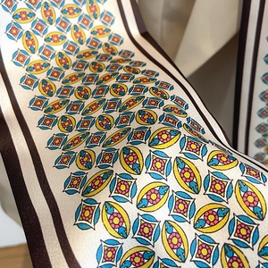 Gros plan d'un foulard en soie élégant aux motifs géo rétro avec bordures marron sur base crème