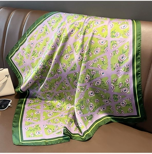 Dettaglio di foulard in seta verde e viola con fiori su un divano in pelle marrone