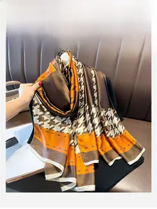 Detailed texture of a houndstooth pattern silk scarf with hand-rolled edges on a leather sofa