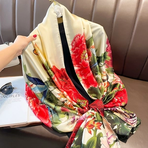 Silky floral scarf with red peonies and blue birds print displayed on a leather sofa