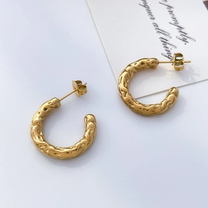 Détail de boucles d'oreilles créoles dorées en C avec texture martelée style lave
