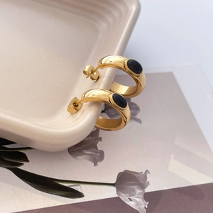 Détail boucles d'oreilles dorées en C avec pierres noires sur une assiette en céramique