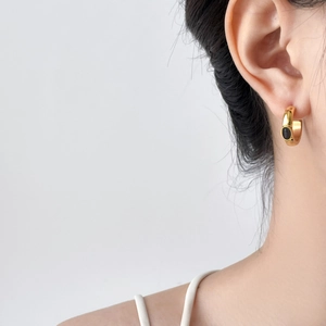 Vue rapprochée d'une boucle d'oreille dorée en C torsadé avec gemme noire