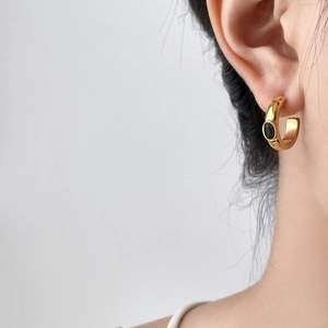Gros plan d'un modèle portant une boucle d'oreille dorée en C avec pierre noire