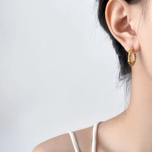 Gros plan de boucles d'oreilles créoles dorées martelées sur un mannequin fond gris épuré