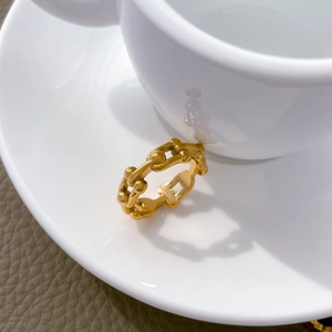 Dettaglio macro dell'anello a catena in oro 18K poggiato sul bordo di una tazza bianca