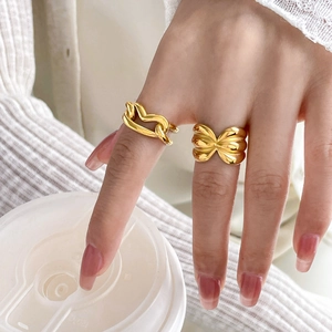 Close-up of chunky gold rings featuring twisted chain and ribbon knot designs on hand