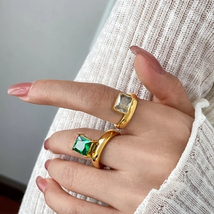 Detail of two chunky 18K gold plated rings with square green and clear zircon stones