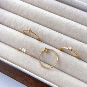 Detailed view of gold twist rings with marquise and square zircon stones on white velvet