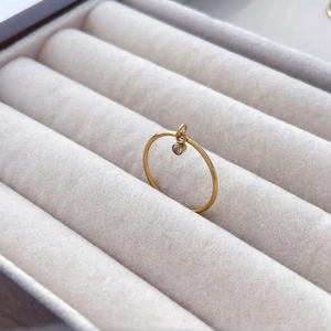 Detail of a thin gold titanium ring featuring a dangling zircon solitaire on gray velvet