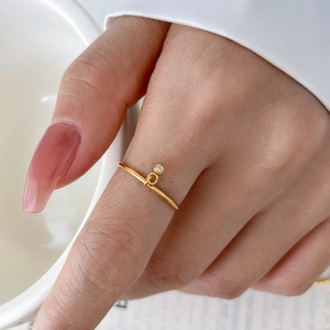 Detail shot of a twisted gold titanium steel ring with a hanging zircon charm on a finger