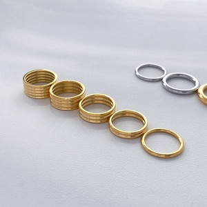 Set of stackable 18K gold and silver plated titanium rings on white leather surface