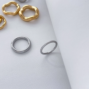 Detail of 18K gold and silver stacked wavy titanium steel rings on white textured surface