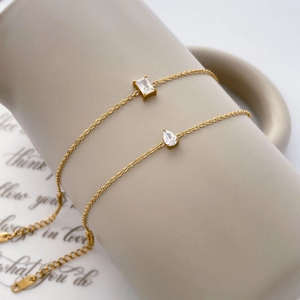 Détail de chaînes dorées 18K avec zircons carrés et en forme de goutte sur céramique