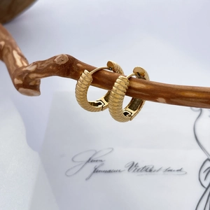 Détail de boucles d'oreilles dorées texturées suspendues à une branche en bois