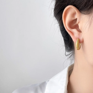 Gros plan d'une boucle d'oreille dorée striée portée par un mannequin