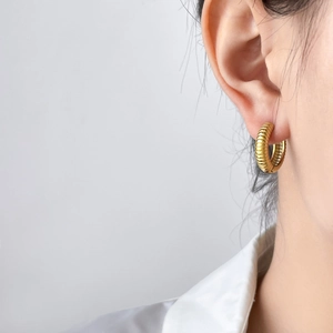 Détail d'une créole dorée avec texture de pneu portée sur le lobe de l'oreille