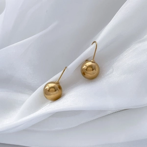 Detailed view of polished golden hollow ball drop earrings on white silk fabric
