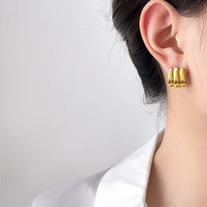 Close-up of golden triple ribbed earrings with high-polish finish on a female model