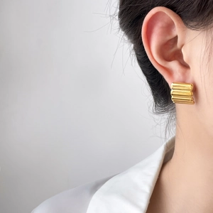 Close-up of golden rectangular textured earrings with horizontal stripes on model