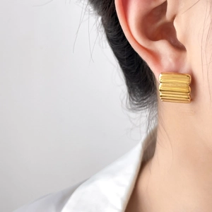 Detailed close-up of golden rectangular earrings with textured horizontal stripes on model