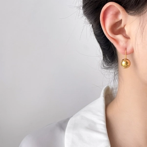 Close-up of minimalist gold hollow ball drop earrings on model with sleek metallic finish