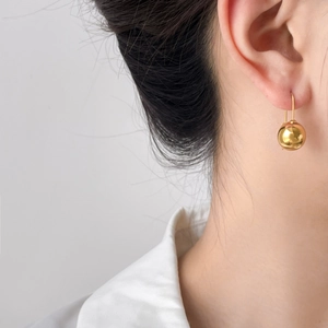 Polished gold hollow sphere drop earrings in titanium steel worn by a model in profile