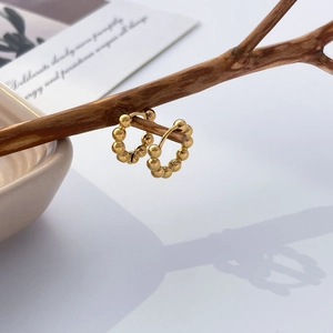 Close-up of golden beaded U-shape earrings hanging on a natural dry wooden branch