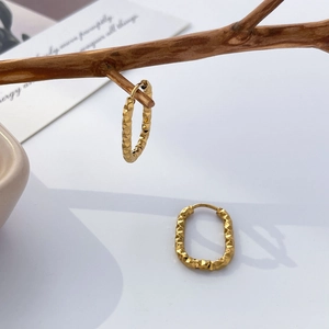 Detail showing 18K gold plated U-shaped earrings with faceted texture on a wooden prop