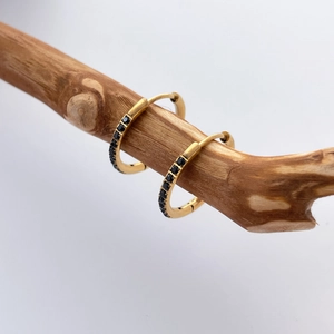 Detail of 18K gold-plated U-shaped hoop earrings with black zircon stones on a branch