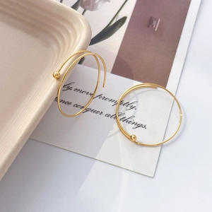 Macro shot of 18K gold plated U-shaped hoop earrings with beads on a ceramic tray