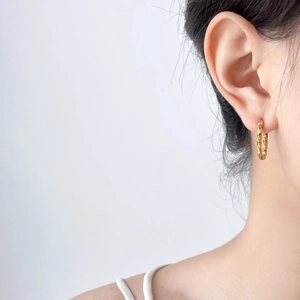 Detail of 18K gold plated U-shaped earrings with geometric faceted texture on earlobe