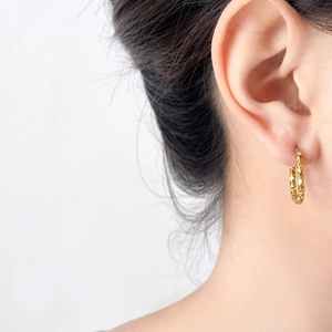 Close-up of gold U-shaped hoop earring with geometric texture on female model's ear