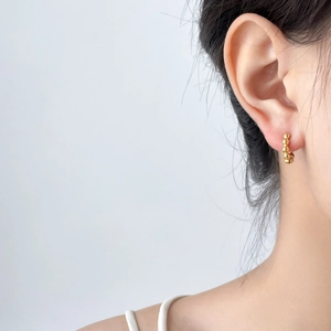 Detail of gold beaded C-shaped earring on model ear with polished metallic finish