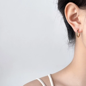 Close-up of gold U-shaped hoop earrings with black zircon stones worn by a model