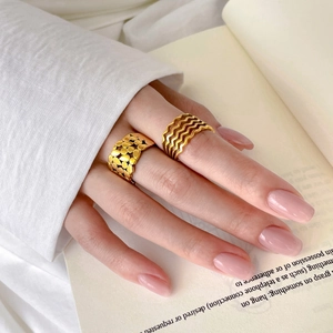Detail of layered gold wave rings and pebble texture band worn on hand against book background