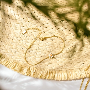 Detailed close-up of a gold daisy charm bracelet with white petals on a straw hat background