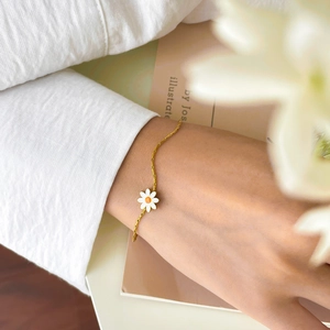 Detail of a gold titanium daisy bracelet worn on a wrist in a soft aesthetic setting