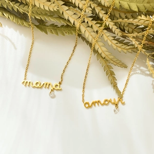 Détail de colliers dorés mama et amour avec accents de zircon sur fond blanc épuré
