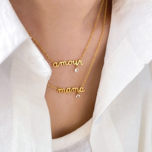 Détail de colliers dorés superposés avec pendentifs 'amour' et 'mama' et zircons