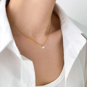 Gros plan d'un collier pendentif en zircon doré porté avec une chemise blanche