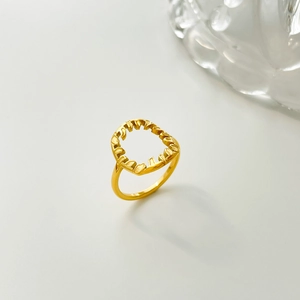 Détail d'une bague florale dorée ajourée irrégulière sur un fond gris clair minimaliste