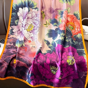 Elegant silk scarf with peony and crane prints, orange border draped on leather