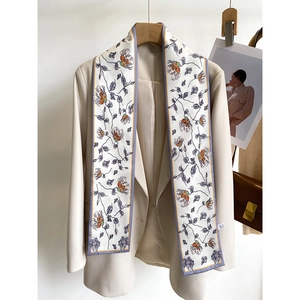 Detailed view of a slim floral silk scarf draped over a beige blazer with flower print