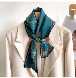 Detail of teal narrow silk scarf with golden ginkgo pattern on beige blazer collar