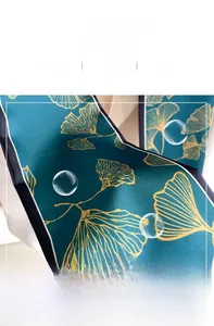 Macro shot of dark green silk scarf featuring golden ginkgo leaves and fine inner stitching