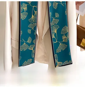 Detail of silk scarf with golden ginkgo leaf pattern draped on a white blazer